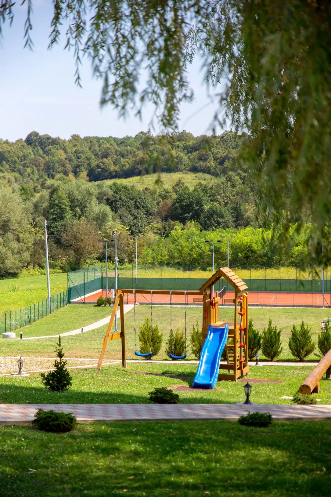 Dječje igralište s toboganom, u pozadini teniski teren